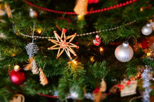 Närbild på en julgran med en mångfald av olika pynt: ljus, glitter, kulor, halmfigurer och kottar. 